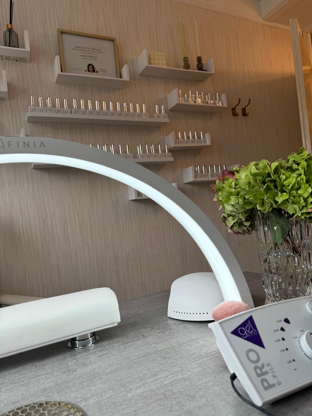 De studio: een witte boogvormige LED-lamp op de behandeltafel, met wandplanken vol gellak en een boeket