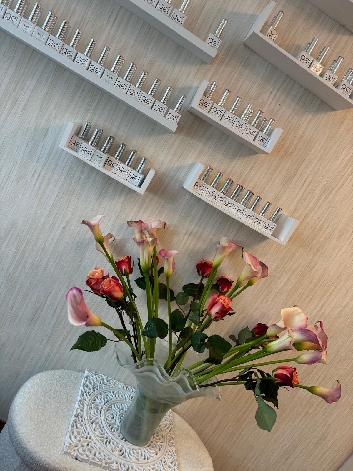 Witte wandplanken met rijen gellak flesjes, met een boeket rozen en lelies op de voorgrond