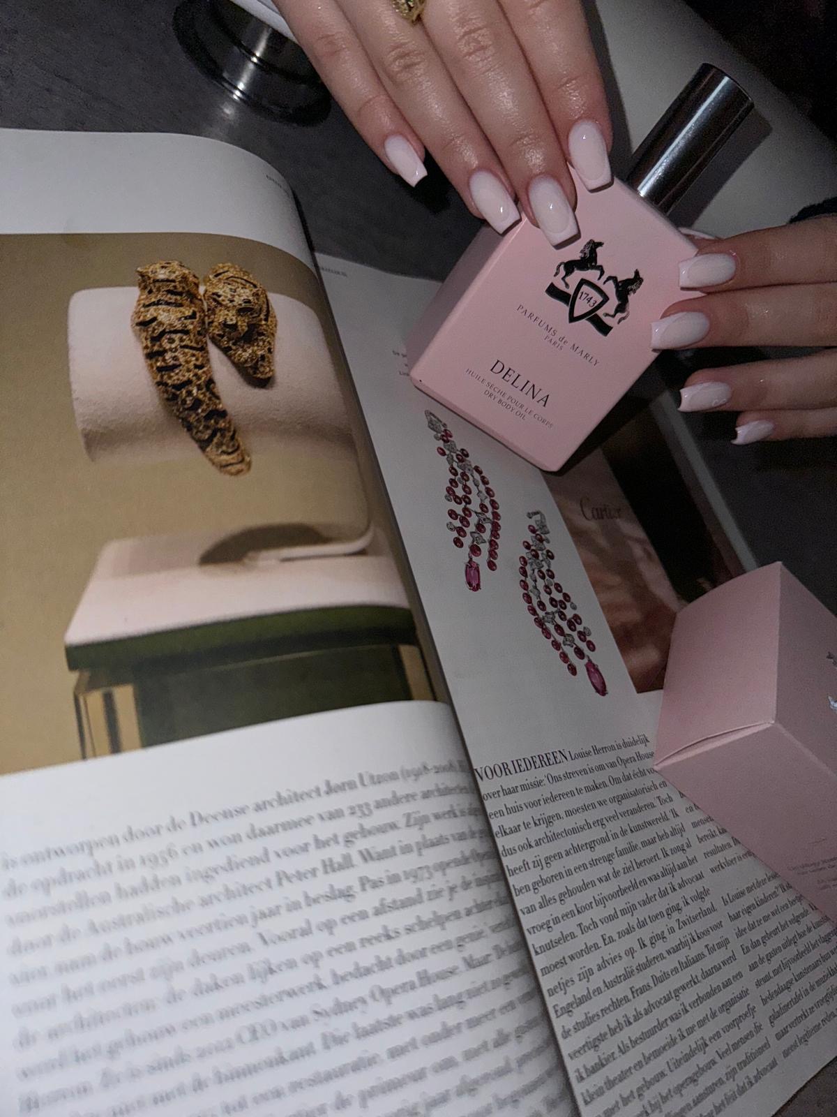 Korte nude nagels, hand houdt een flesje vast boven een tijdschrift