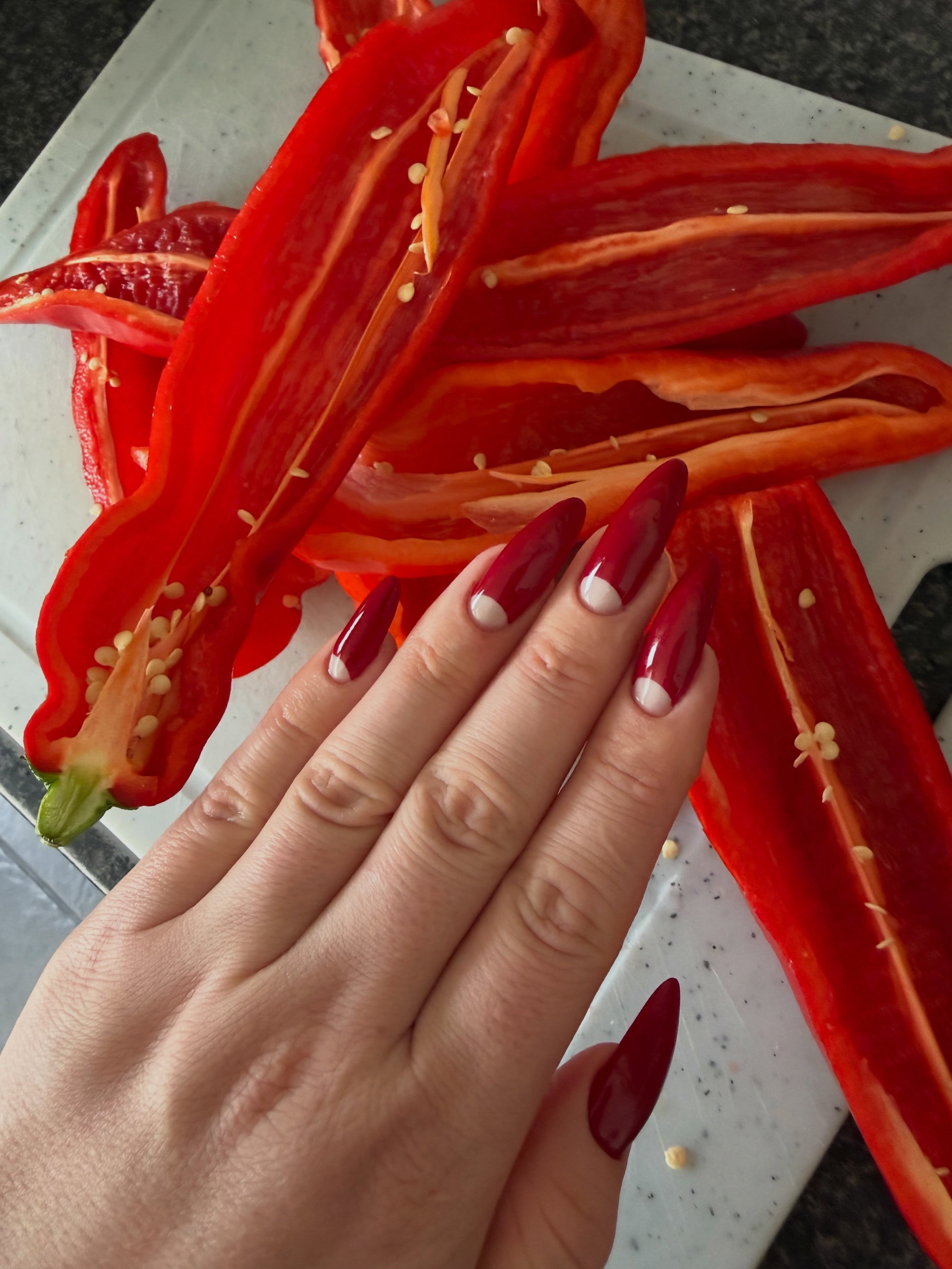 Lange dieprode almond nagels met een witte halve maan, op een rood decor